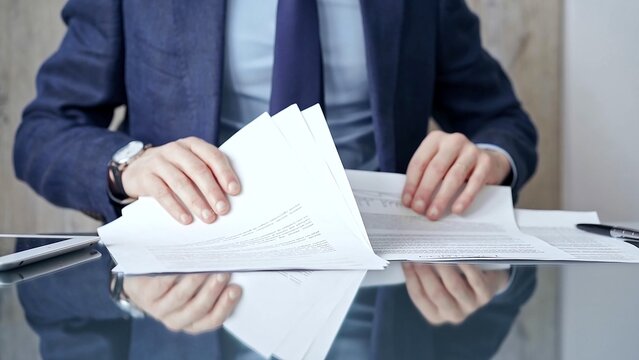 Businessman reviewing documents at office desk. Close-up of a professional man's hands examining paperwork with pen and tablet in sight. Business people concept