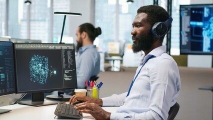 Fototapeta premium Software developer testing generative AI machine learning algorithms and listening music at work. African american man wearing headphones scaling productivity with AI large language model, camera A