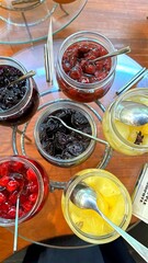 Glass jars brimming with an assortment of jams and vibrant fruit salad adorn a breakfast buffet table, inviting hotel guests to indulge in a delightful morning treat