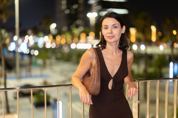 Fototapeta premium Happy young woman leaning on metal railing against background of blurred city lights of Barcelona
