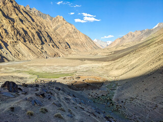 Aerial view of traditional stone sheep pens with flocks of goats and sheep in the remote Ghujerav Valley, Shimshal, Pakistan. The image captures the rugged mountain terrain, riverbed, and pastoral...