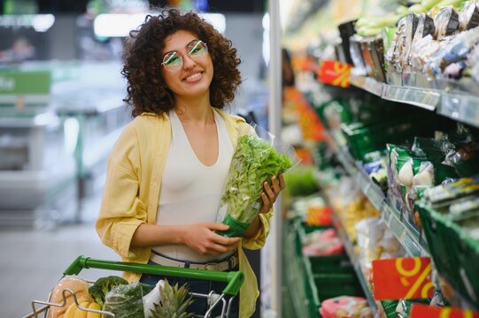 Young woman choosing fresh lettuce in supermarket - Powered by Adobe