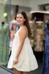 Naklejka premium Young girl in white dress is looking for something at street market - looking at the goods with interest