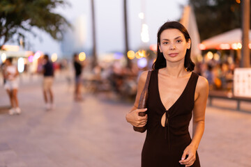 Obraz premium In evening, smiling girl walks around old city district Barceloneta, pedestrian promenade embankment. People are walking by. Person in city, city bustle. Carefree, promenade