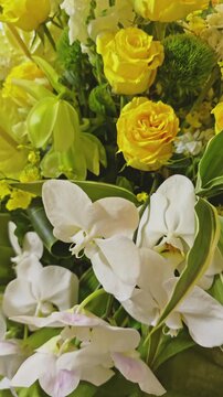 Close-up of a vibrant floral arrangement with yellow roses, white orchids, and green foliage. Perfect for themes of weddings, celebrations, spring, and nature.