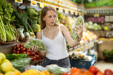 Blonde woman stands near a vegetable counter in a store and chooses edamame. Customer looks at the green beans and checks them before buying