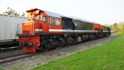 Fototapeta premium Powerful Indonesian locomotive pulling a container train along the railway tracks, with a clear sky and lush greenery on both sides