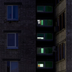 Dark brick residential building at night with glowing windows, showing glimpses of interior lights and shadows behind the glass.