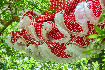 Close-up of a red flamenco dress with white polka dots and ruffled white trim hanging among green leaves, vibrant and traditional.