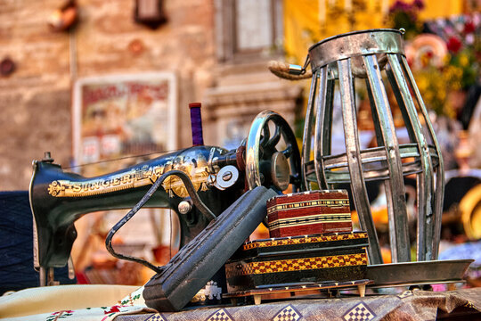 A vintage Singer sewing machine with ornate details is displayed alongside a metal frame and decorative boxes during the Crosses of May in Granada. Craft, tradition.