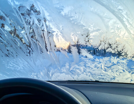 Stunning frost patterns cover a car windshield on a cold winter morning, revealing intricate ice crystals and a serene view. Perfect for seasonal themes.