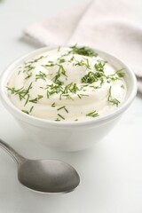 Delicious yogurt in bowl, dill and spoon on white table, closeup