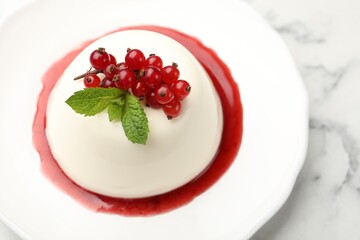 Delicious panna cotta with red currants, sauce and mint on white marble table, closeup