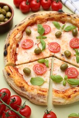 Delicious cut pizza and ingredients on light green background, closeup