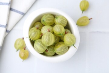 Fresh green gooseberries in bowl on white table, top view