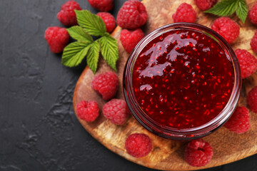 Sweet raspberry jam in glass jar and berries on gray textured table, top view