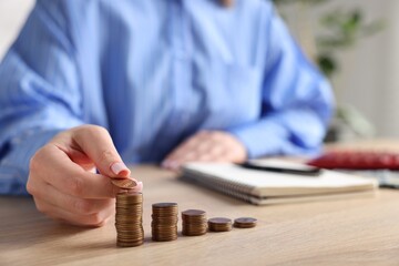 Woman stacking coins at wooden table, closeup