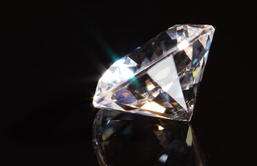 One shiny diamond on mirror surface against black background, closeup