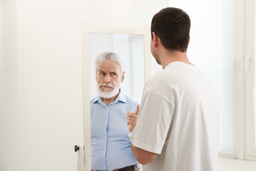 Obraz premium Man seeing himself as elder in mirror. Conceptual collage about past and future, flow of time, age