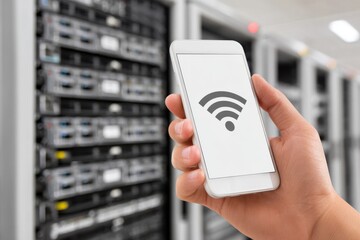 Hand holding smartphone displaying wifi symbol, in server room with blurred background, suggesting network connectivity.