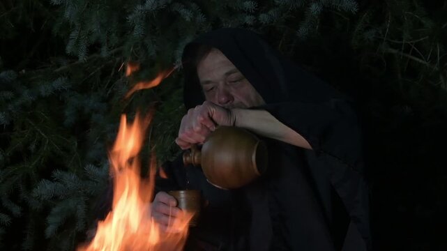 a monk in a hooded cloak pours wine from a jug 1