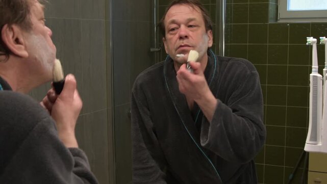 an elderly man in a bathrobe looks in the mirror