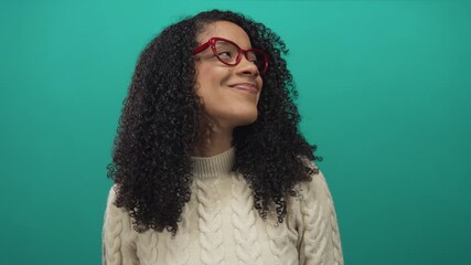 Woman with curly hair wearing red glasses and subtle smile looking sideways in teal studio; confidence curiosity. - Powered by Adobe