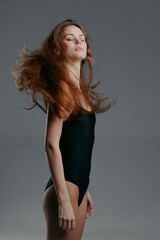 Fototapeta premium Young woman in black bodysuit with flowing hair posing confidently against gray background.