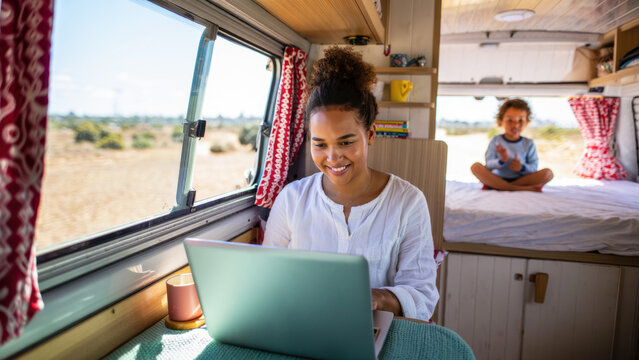 Remote working mom in campervan, digital nomad family lifestyle, laptop workspace with child, vanlife with kids, mobile home office, family travel scene, homeschooling on the road