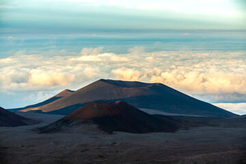 Volcanic cinder cones at the summit of Mauna Kea on the Big Island of Hawaii, rising above the clouds in the soft light of sunset.