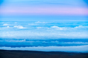 Volcanic cinder cones at the summit of Mauna Kea on the Big Island of Hawaii, rising above the clouds in the soft light of sunset.