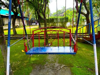 Colorful swing hangs over the lush moss covered ground in a playground surrounded by nature