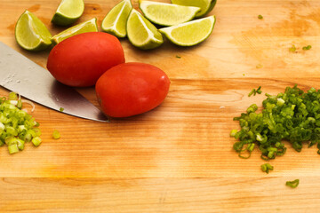 Closeup of Cutting Board with Knife, Scallions, Limes, and Tomatoes