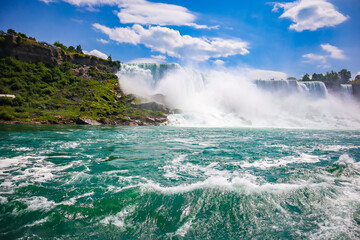The gushing turquoise water from the Niagara falls with blue sky and white clouds the beautify scenry of nature