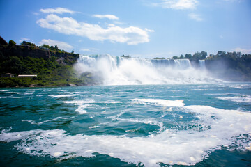 The gushing turquoise water from the Niagara falls with blue sky and white clouds the beautify...