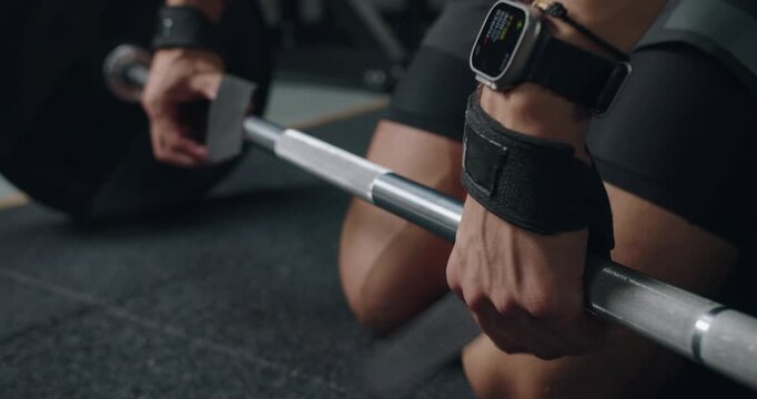 Close-up of a man's hands gripping a barbell in a gym setting, focusing on smartwatch data during weightlifting. Fit Man During Intense Gym Training Session with Smartwatch