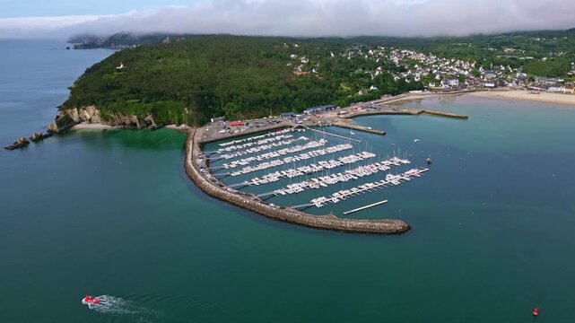 Drone pulling back over Morgat marina in Crozon, showing the harbor, breakwater, coastline, vegetation and distant houses - Brittany France