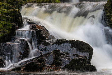 Fototapeta premium Flowing waterfall streams down over dark rocks in a woodland setting