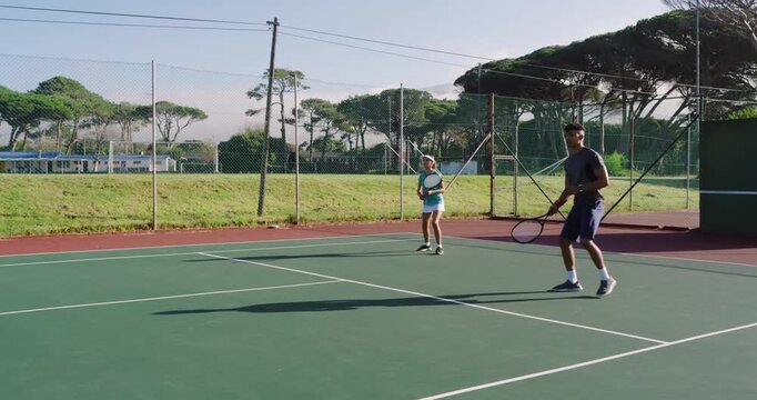 Tossing ball prompting Asian man and White woman partners volleying for drill on hard court