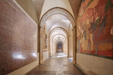 Medieval Stone Cloister With Latin Inscriptions And Frescoed Walls At Montserrat Monastery. Gothic arches, religious art, historical corridor, pilgrimage site, spiritual heritage, Catalonia Spain