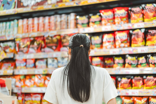 Rear view young adult asian woman customer choosing snack food from shelf shopping at asia supermarket