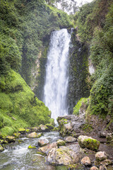 Majestic Peguche waterfall in Otavalo, Ecuador. Water cascades powerfully among moss-covered rocks and vibrant greenery, reflecting the purity of Andean nature.