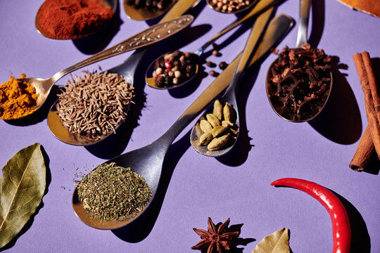 Horizontal image of large numbers of spoons with spices on them for cooking food isolated on purple background