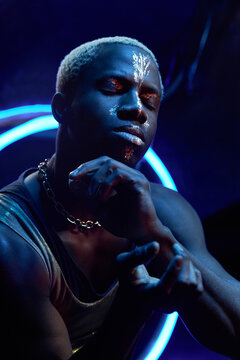 Vertical high angle medium studio portrait of modern young Black man wearing casual outfit with paint on his face posing on camera moving his hands