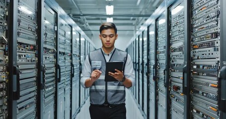 Young IT technician diligently checks server status on tablet in modern data center with rows of equipment - Powered by Adobe