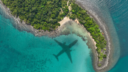 Aerial view of shadow passenger plane silhouette and sandy beach blue sea with waves at sea beach summer vacation sea travel concept