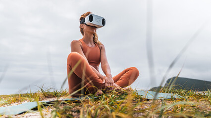 Woman practicing meditation outdoors in yoga pose while wearing VR headset. Concept of digital wellness, relaxation, balance, future technology and mindfulness with virtual reality in nature.