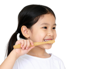 A young girl smiles while brushing her teeth with a wooden toothbrush against a black background, promoting dental hygiene and healthy habits.