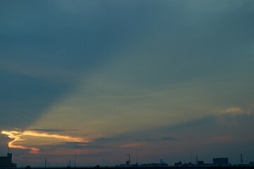 Fototapeta premium 曇り空の切れ間からオレンジ色の光を放つ夕暮れの太陽。