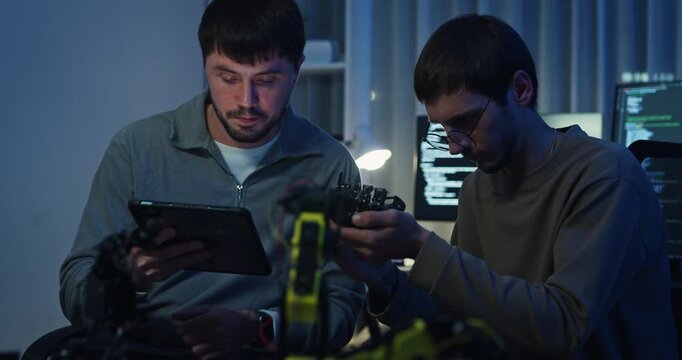 Team adult male engineer collaborate on robotic hand project using AI code solutions machine learning at tech workspace night. Artificial intelligence interface, collaboration prototype development.